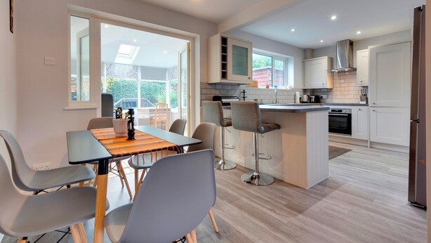 Een moderne keuken met een centraal eiland, barstoelen en een eethoek met een tafel en stoelen.