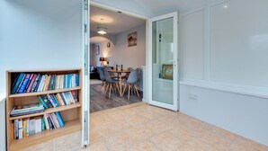 Een moderne woonkamer met een boekenkast, een eethoek met een tafel en stoelen, en een glazen deur die naar een andere kamer leidt.