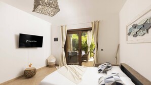 Une chambre à coucher comprenant un lit, une télévision, un panier en osier et donnant sur un espace extérieur avec une table et des chaises.
