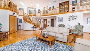 Un salon spacieux avec un escalier en bois, un canapé beige et un tapis à motifs.
