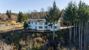 Une maison à deux étages dotée d’une grande terrasse, entourée d’une forêt dense et de nombreux arbres.