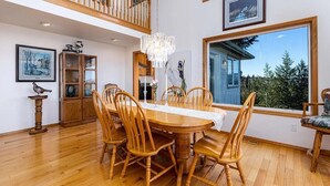 Un coin repas avec une table et des chaises en bois, un lustre et une grande fenêtre donnant sur les arbres.