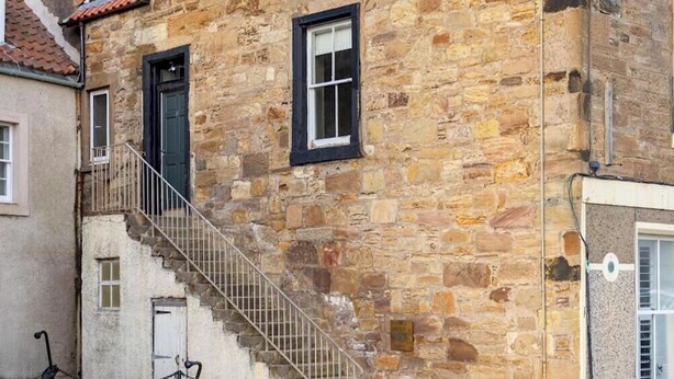 A stone building with a staircase leading to the entrance, a small window, and a door. - Ledger's Cottage- Harbourfront Home Pittenweem (Pittenweem)