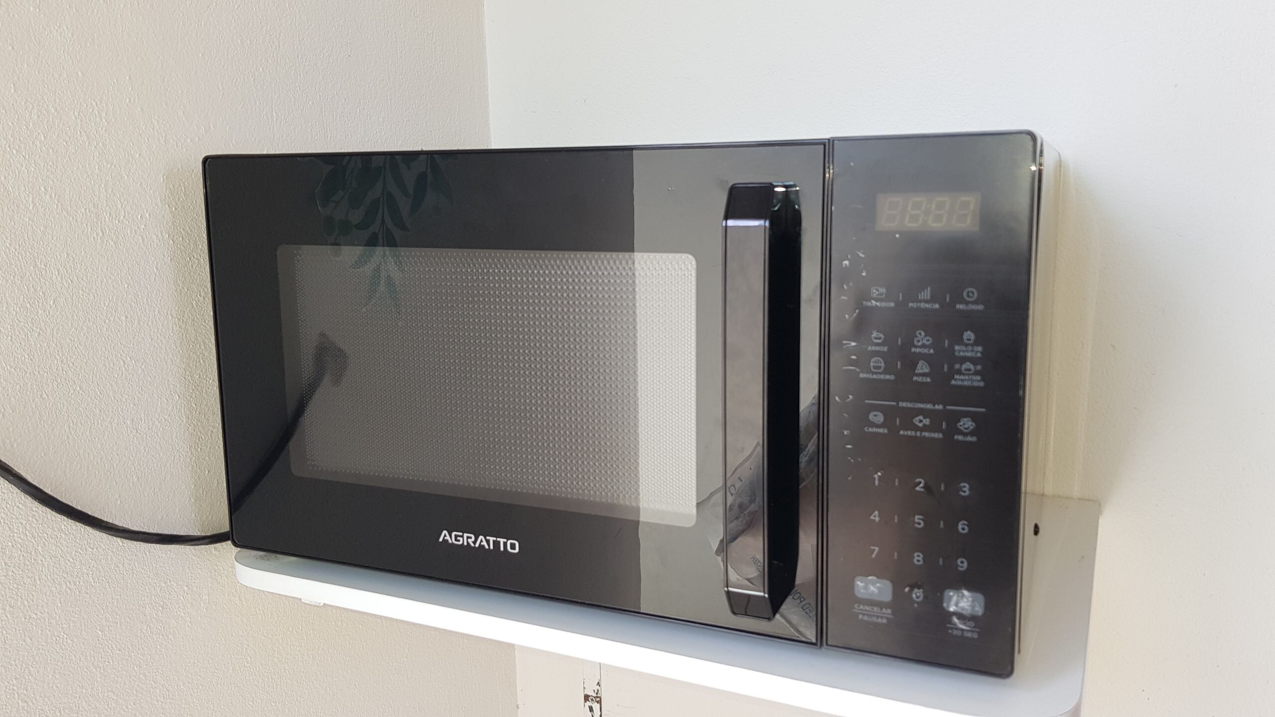Un horno microondas negro con pantalla digital y panel de control, fijado a una pared blanca.