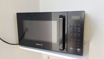 Un horno microondas negro con pantalla digital y panel de control, fijado a una pared blanca.
