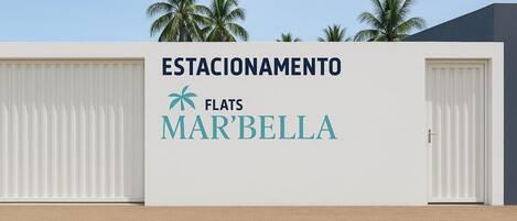 A building with a sign reading 'ESTACIONAMENTO FLATS MARBELLA' and two closed doors.