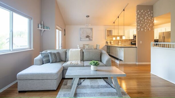 A modern living room with a grey sectional sofa, a wooden coffee table, and a view of the kitchen and dining area. - The Last Frontier Lake House Lodge in Anchorage 3bdrm 2ba (Anchorage)