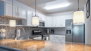 A modern kitchen with white cabinets, a stainless steel refrigerator, a microwave, a gas stove, and a large island with a granite countertop. - The Last Frontier Lake House Lodge in Anchorage 3bdrm 2ba (Anchorage)