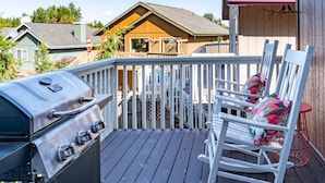 A deck with a barbecue grill and two rocking chairs with colorful cushions. - The Last Frontier Lake House Lodge in Anchorage 3bdrm 2ba (Anchorage)