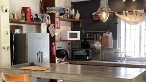 Una cocina con una isla grande, electrodomésticos de acero inoxidable y varios utensilios de cocina en las estanterías.