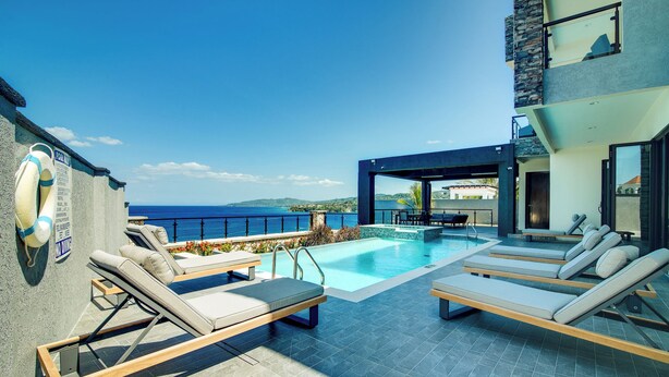 A pool area with lounge chairs, a lifebuoy, and a view of the sea. - Luxury Oceanfront Villa~ Fully Staffed~Pool~Jacuzzi~Movie Theatre (tower isle)