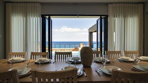 A dining table set for six with chairs, a vase centerpiece, and a view of the ocean through open doors. - Luxury Oceanfront Villa~ Fully Staffed~Pool~Jacuzzi~Movie Theatre (tower isle)