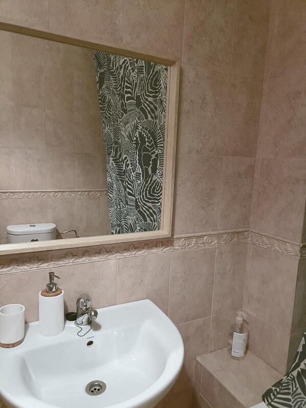 Un baño con lavamanos blanco, espejo y cortina de ducha estampada.
