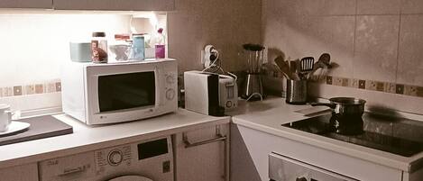A compact kitchen with a washing machine, microwave, toaster, and a stove.
