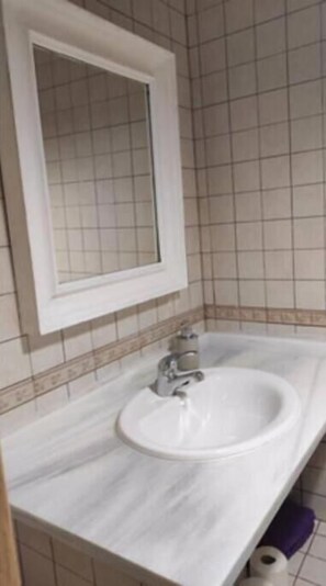 Ein Badezimmer mit einem weißen Waschbecken, einem Spiegel darüber und einer gefliesten Wand.