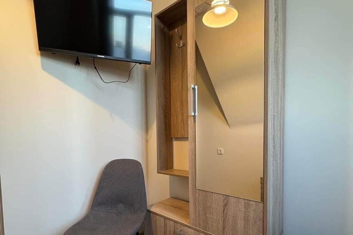 A room with a TV mounted on the wall, a wooden wardrobe with a mirror, and a chair.
