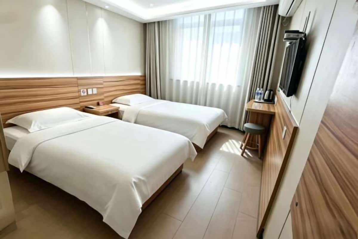 Hotelkamer met twee bedden, een televisie, een kleine tafel met een krukje, en een raam met gordijnen.