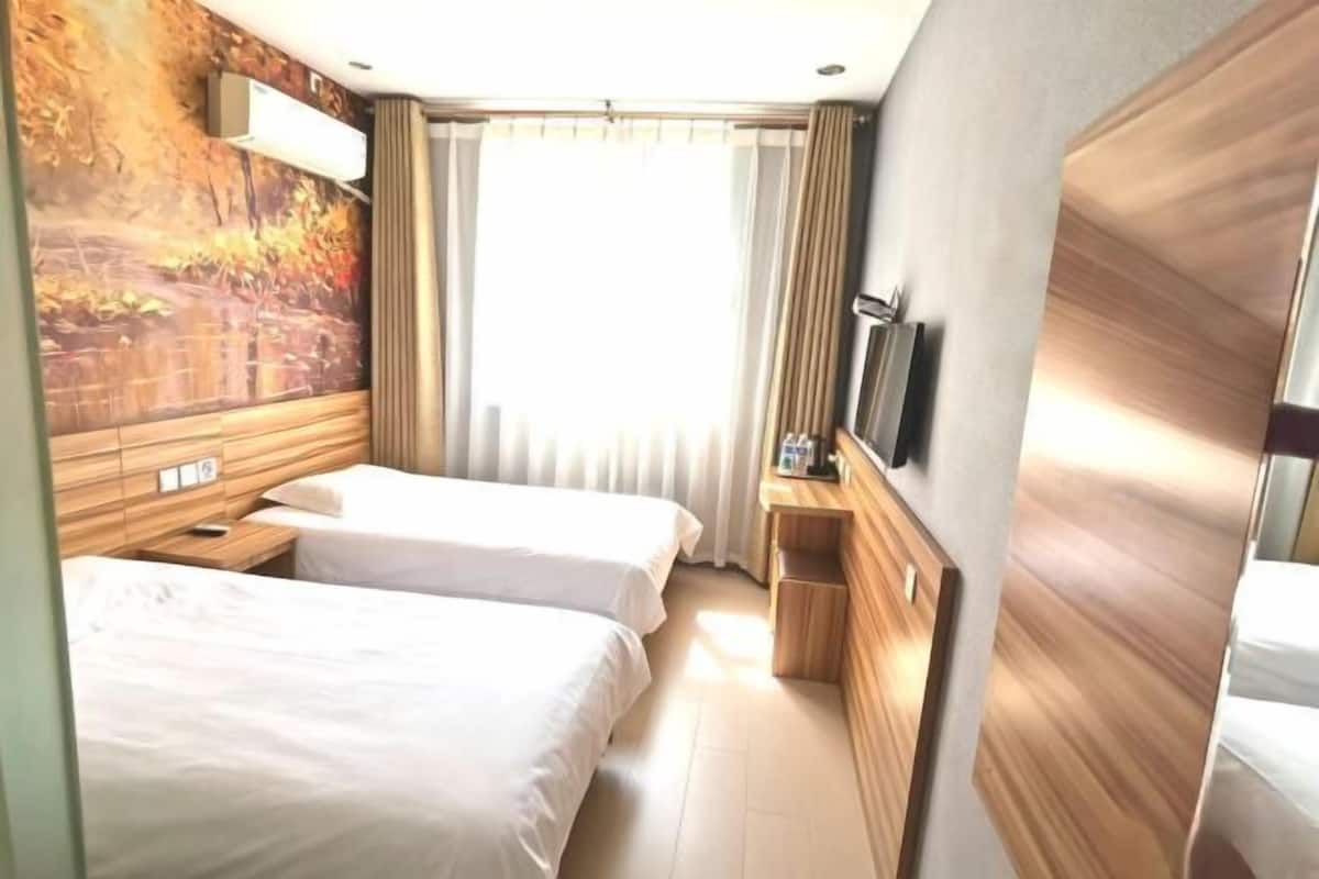 Een hotelkamer met twee bedden, een houten hoofdbord, een televisie en een groot raam met gordijnen.