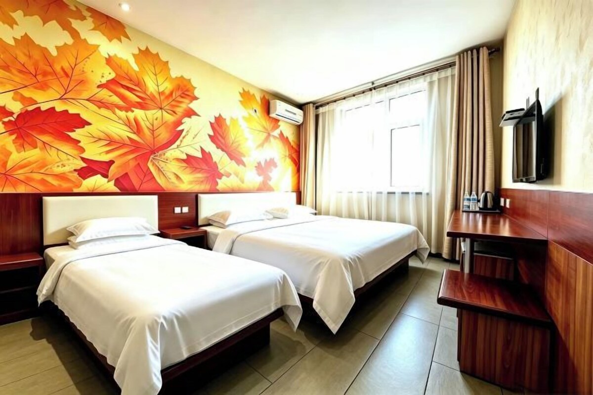 Une chambre d’hôtel avec deux lits, un bureau en bois, une télévision et une grande fenêtre avec des rideaux.
