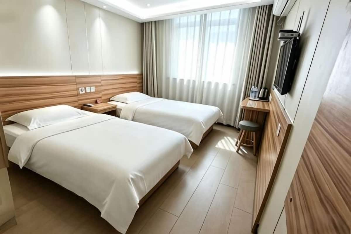Een hotelkamer met twee bedden, een bureau, een stoel, een televisie en een raam met gordijnen.