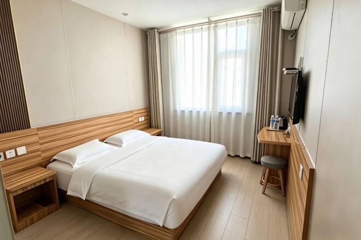 Een hotelkamer met een bed, bureau, stoel, televisie en een raam met gordijnen.