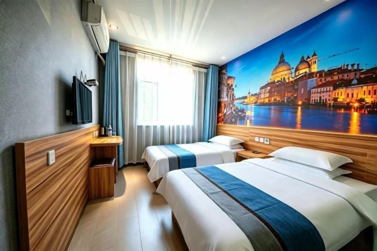 Une chambre d’hôtel avec deux lits, une télévision, une fenêtre avec des rideaux et une fresque représentant un paysage urbain sur le mur.