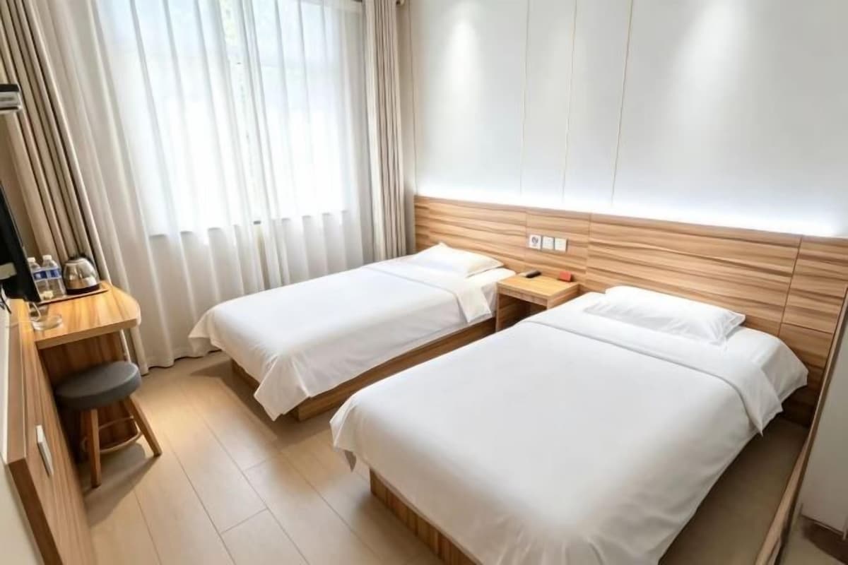 Et hotelværelse med to senge, et skrivebord med stol og et vindue med gardiner.