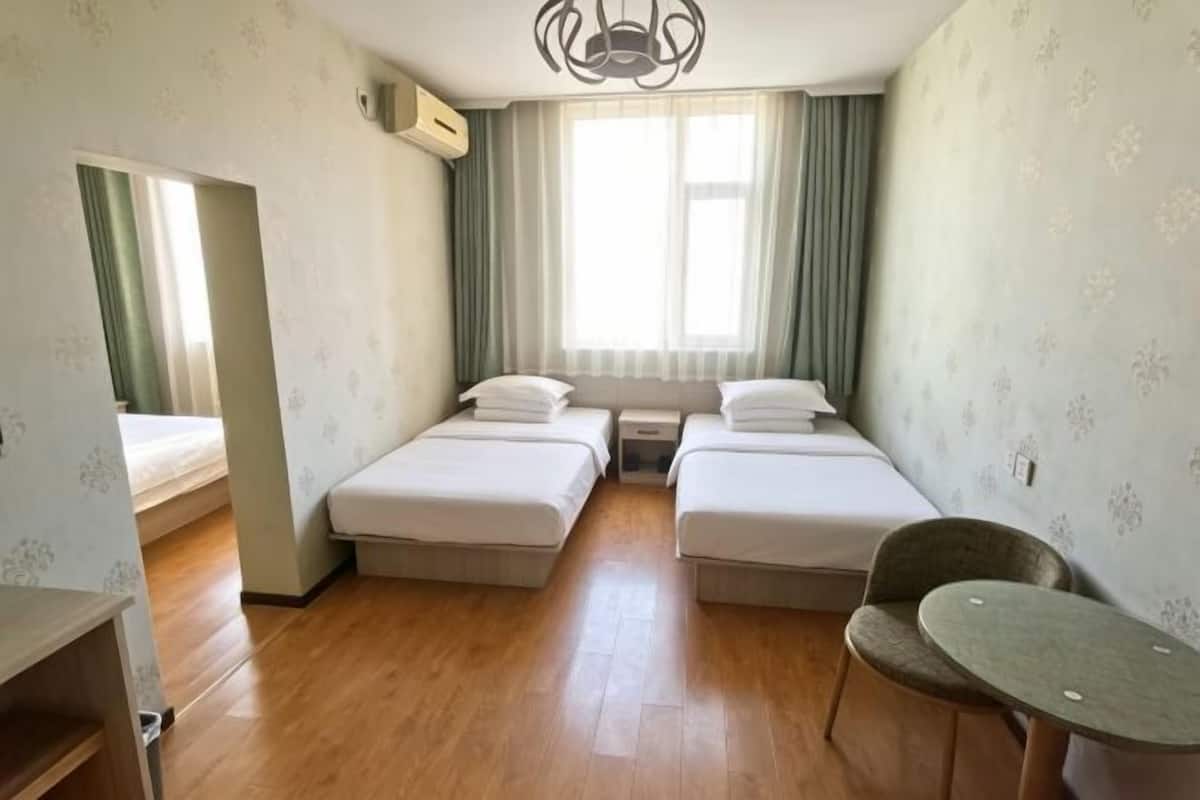 Een kamer met twee bedden, een tafeltje, een stoel en een raam met gordijnen.