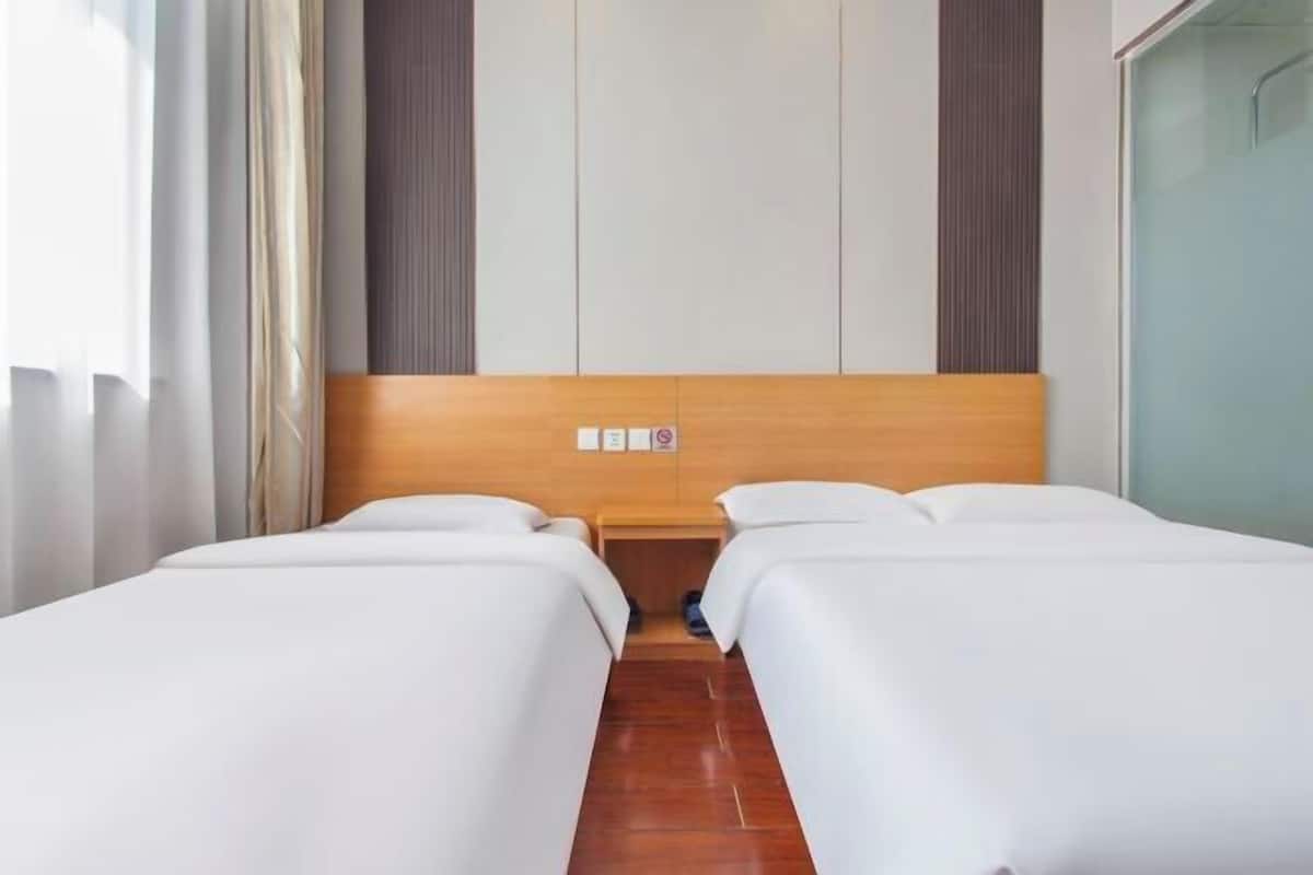 Een hotelkamer met twee bedden, een houten hoofdbord, een klein nachtkastje en een douchecabine met glazen wanden.