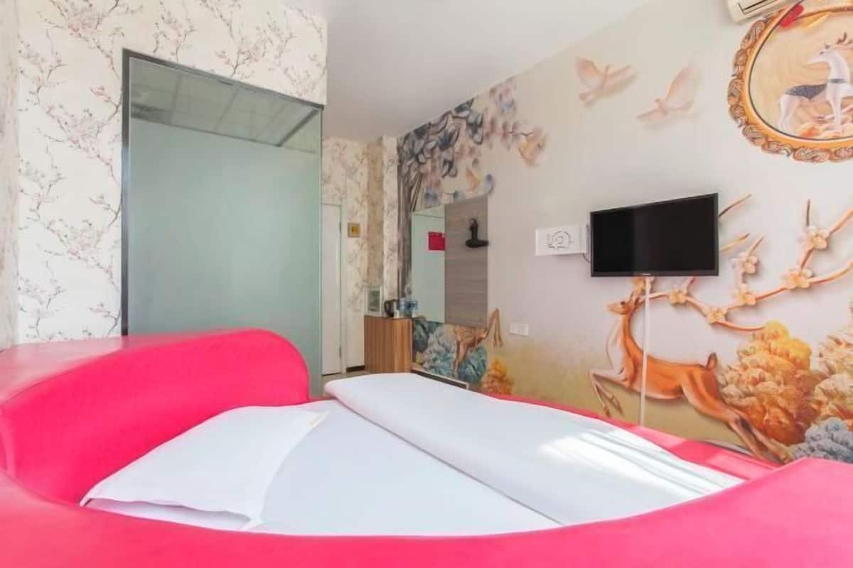 Een kamer met een rode bank, een bed met witte beddengoed, een aan de muur bevestigde televisie en een muurschildering met herten en vogels.