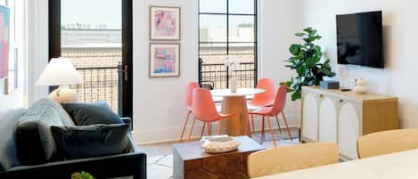 Una sala de estar moderna con sofá, una mesa de comedor con sillas, un televisor montado en la pared y un balcón con vistas.