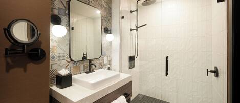 A modern bathroom with a large mirror, a sink, and a shower.