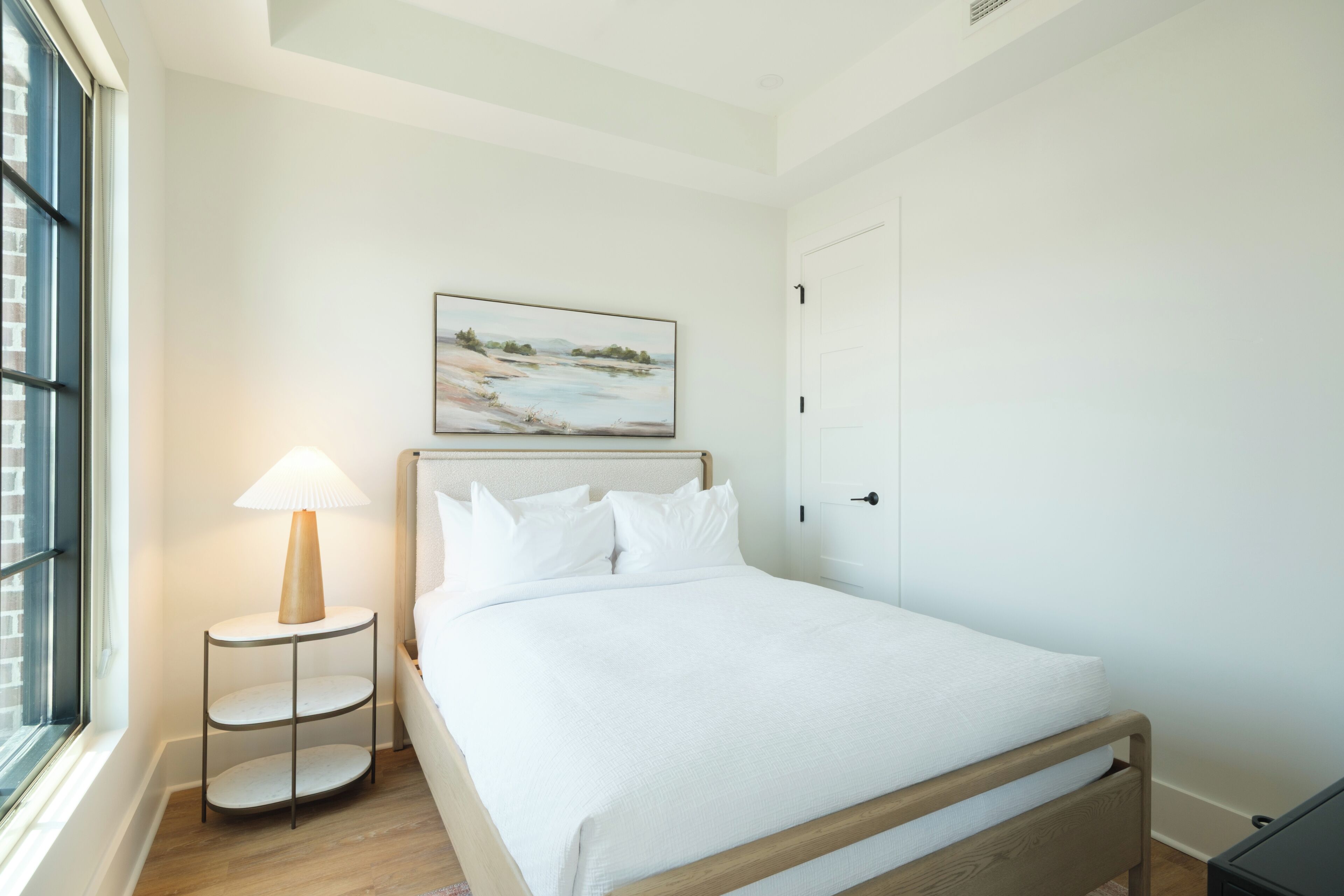 Quarto de hotel com uma cama, abajur, quadro e janela.
