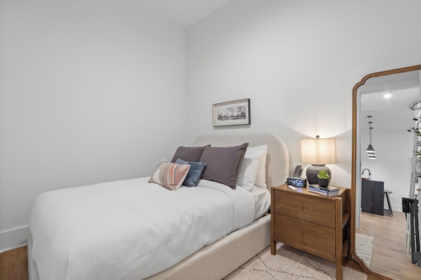 Une chambre à coucher avec un lit, une table de chevet, une lampe, une horloge et un tableau encadré au mur.