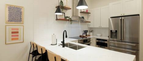 Een moderne keuken met een centraal eiland, roestvrijstalen apparatuur en een witte betegelde spatwand.