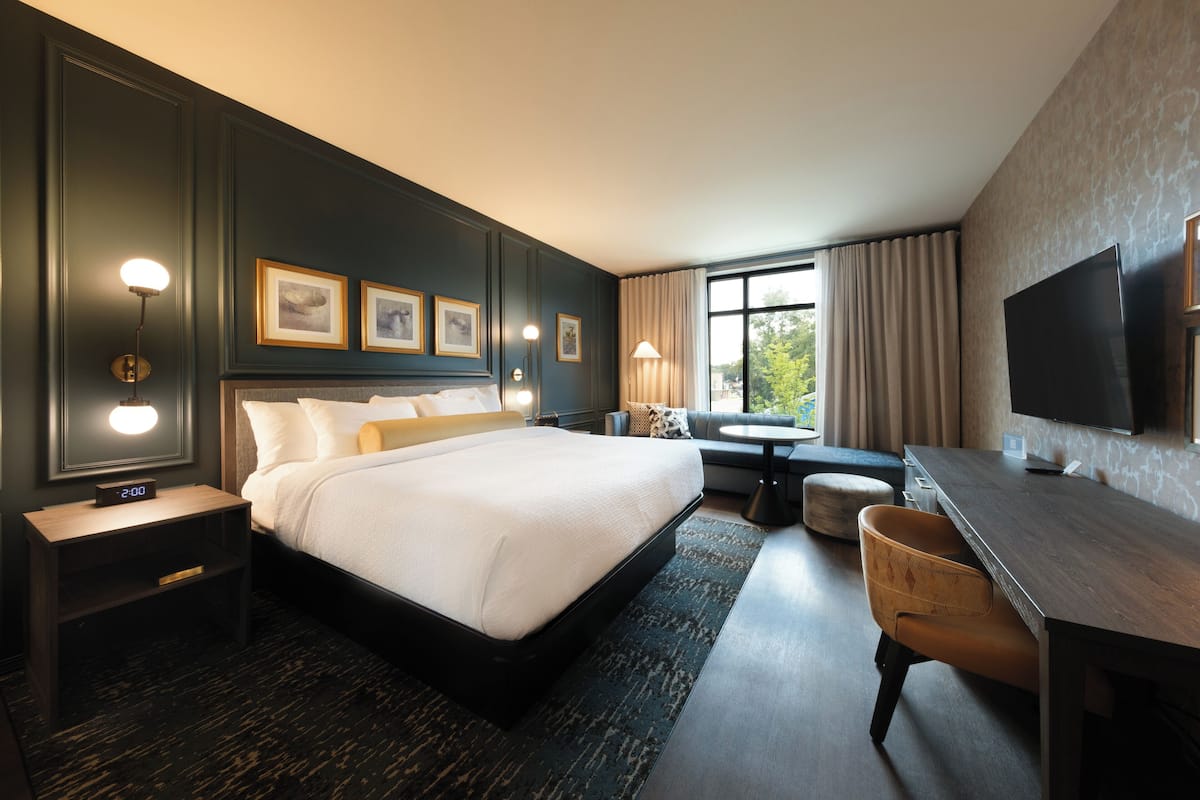 A hotel room with a large bed, a desk, a chair, a TV, and a window with curtains.