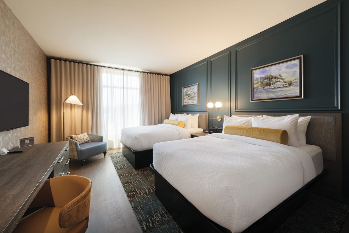 A hotel room with two beds, a desk, a chair, and a television.