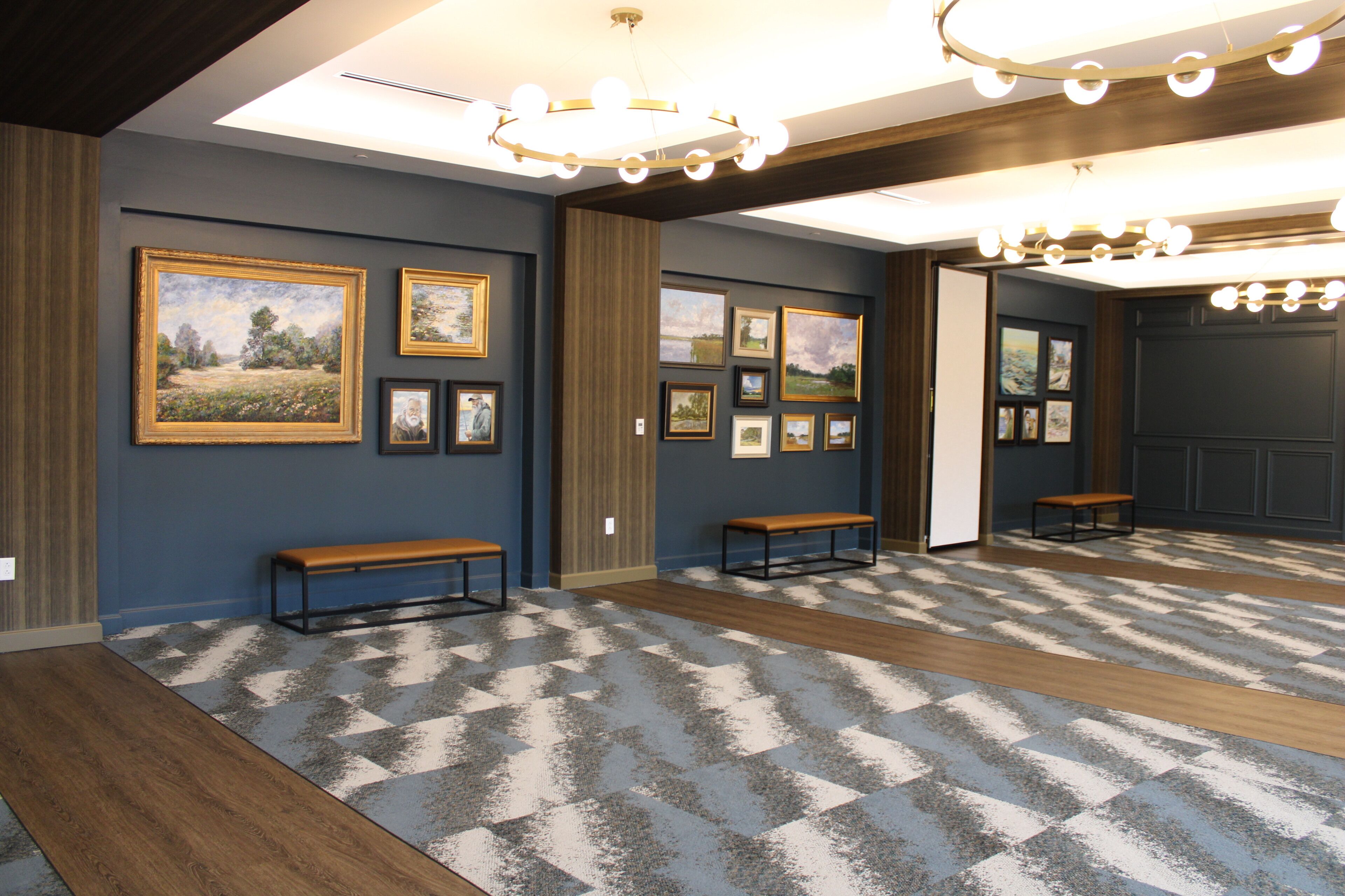 A hallway with framed pictures on the walls, wooden benches, and a patterned carpet.