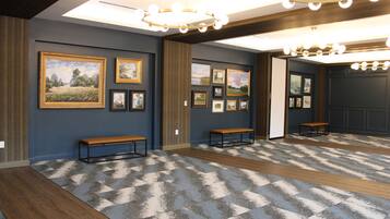 A hallway with framed pictures on the walls, wooden benches, and a patterned carpet.