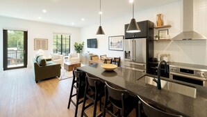 A modern kitchen with a large island, stainless steel appliances, and a dining area with a sofa and chairs. - OS Hotel  (Ocean Springs)