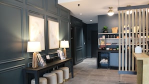 A modern lobby with a dark blue wall, a reception desk, a seating area with ottomans, and a decorative wooden partition. - OS Hotel  (Ocean Springs)