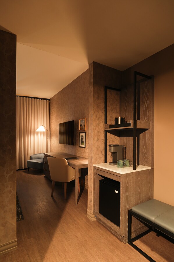 Quarto de hotel com escrivaninha, cadeira, televisão, prateleiras e um banco.