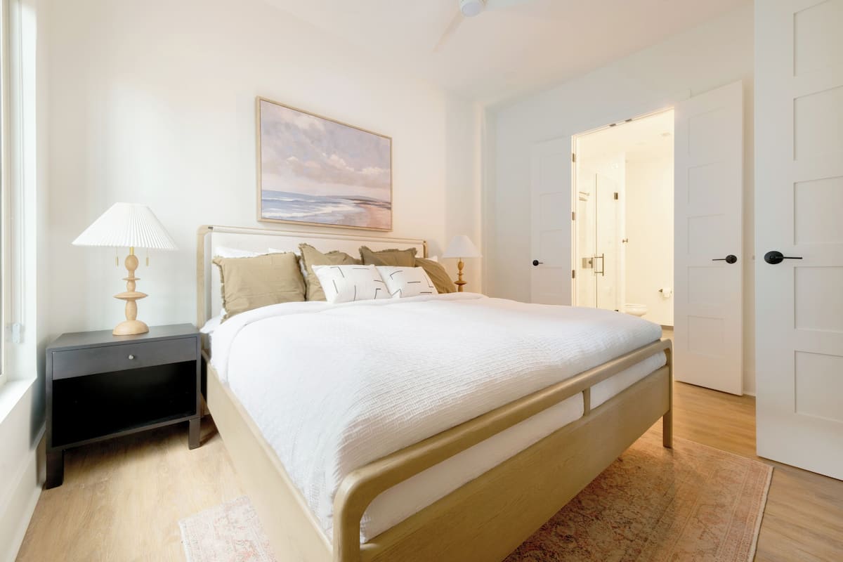 A bedroom with a bed, nightstand, lamp, and a painting on the wall.
