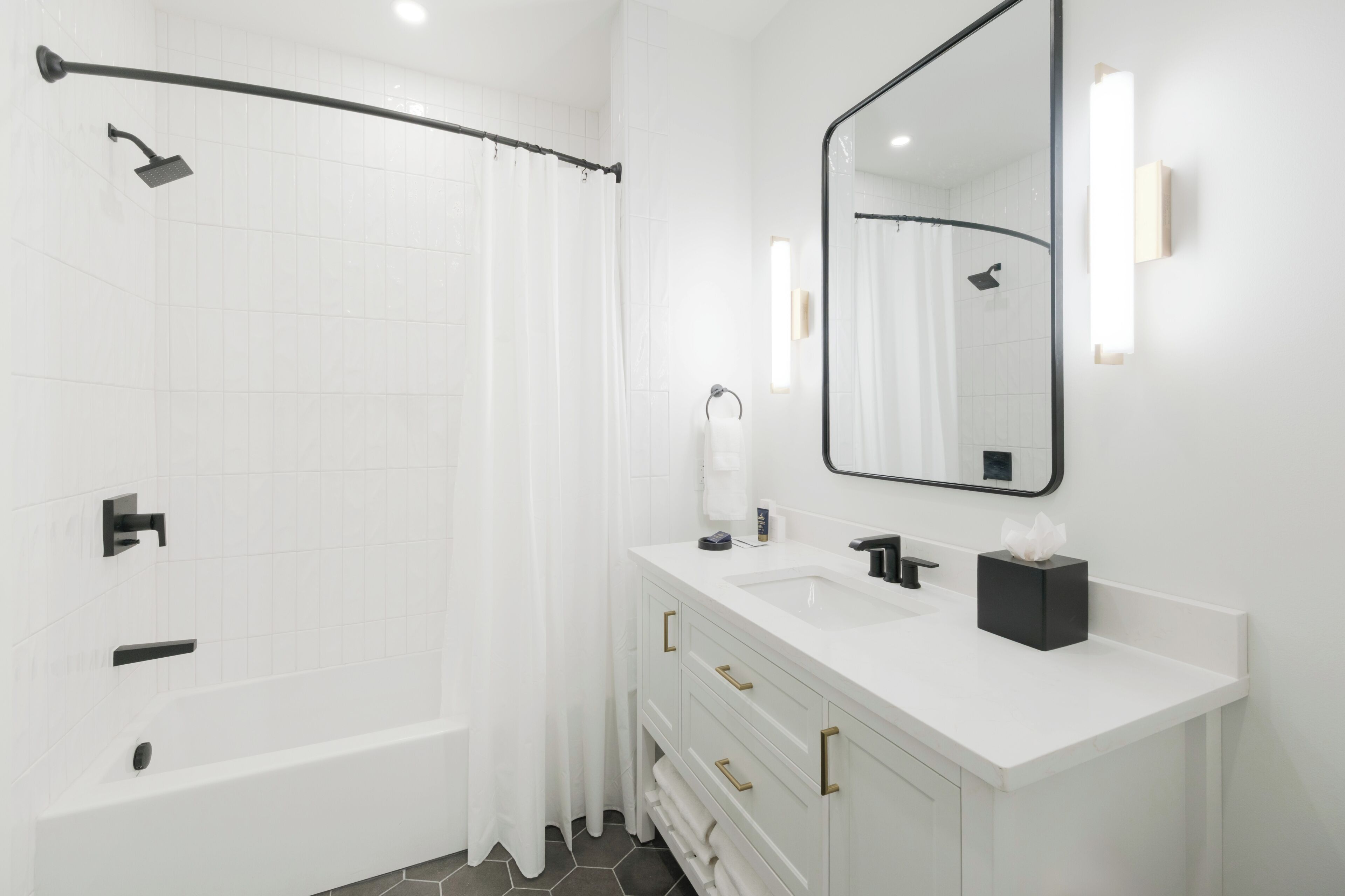 Un baño moderno con bañera, ducha, tocador blanco con espejo y un perchero para toallas.