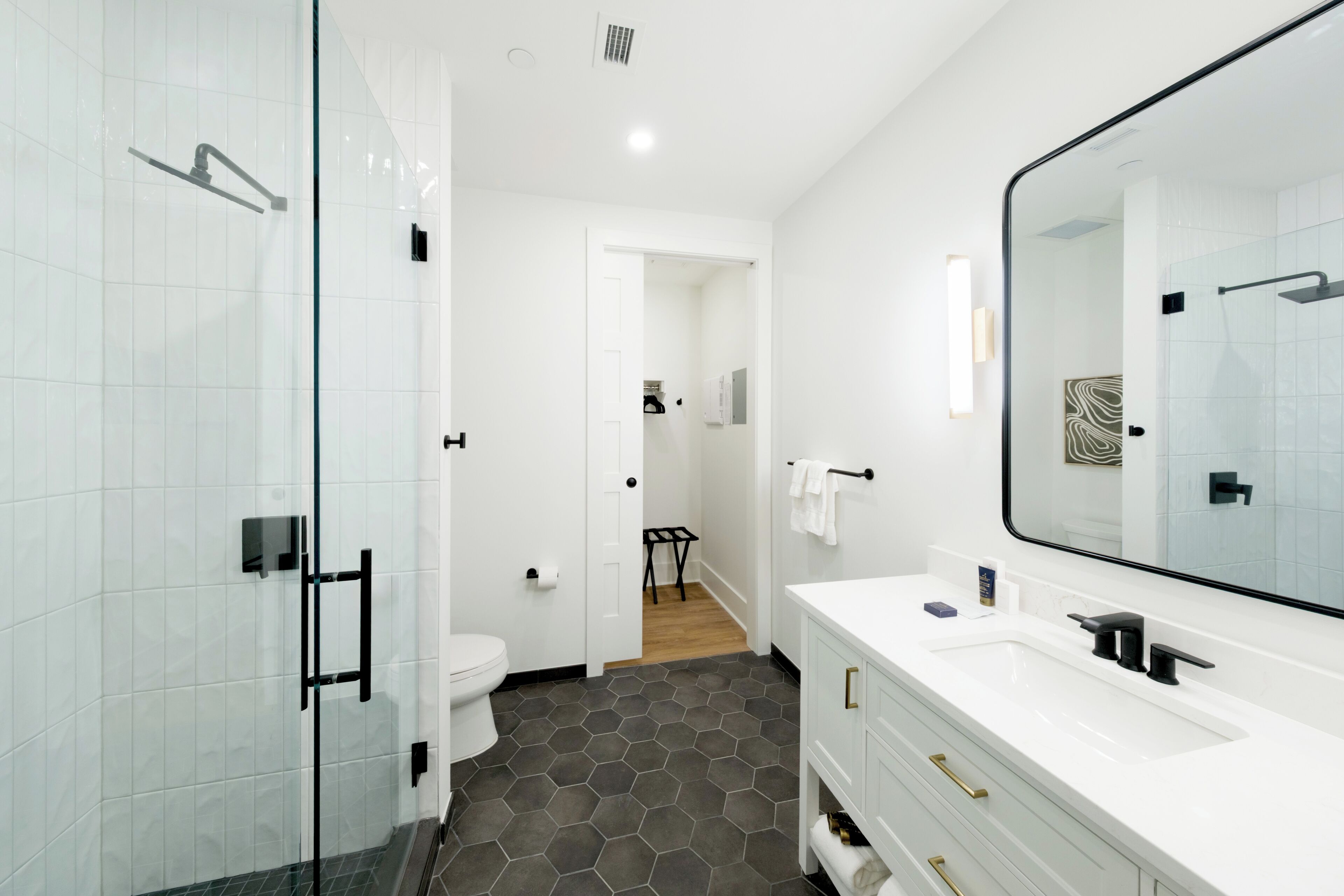 Un baño moderno con cabina de ducha de vidrio, un lavamanos blanco con detalles dorados y un espejo grande.