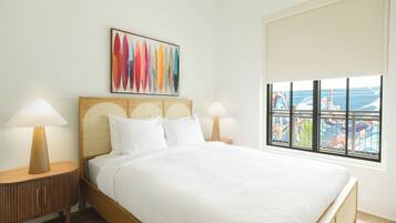 A hotel room with a bed, two bedside tables, a window with a view, and a colorful abstract painting on the wall.
