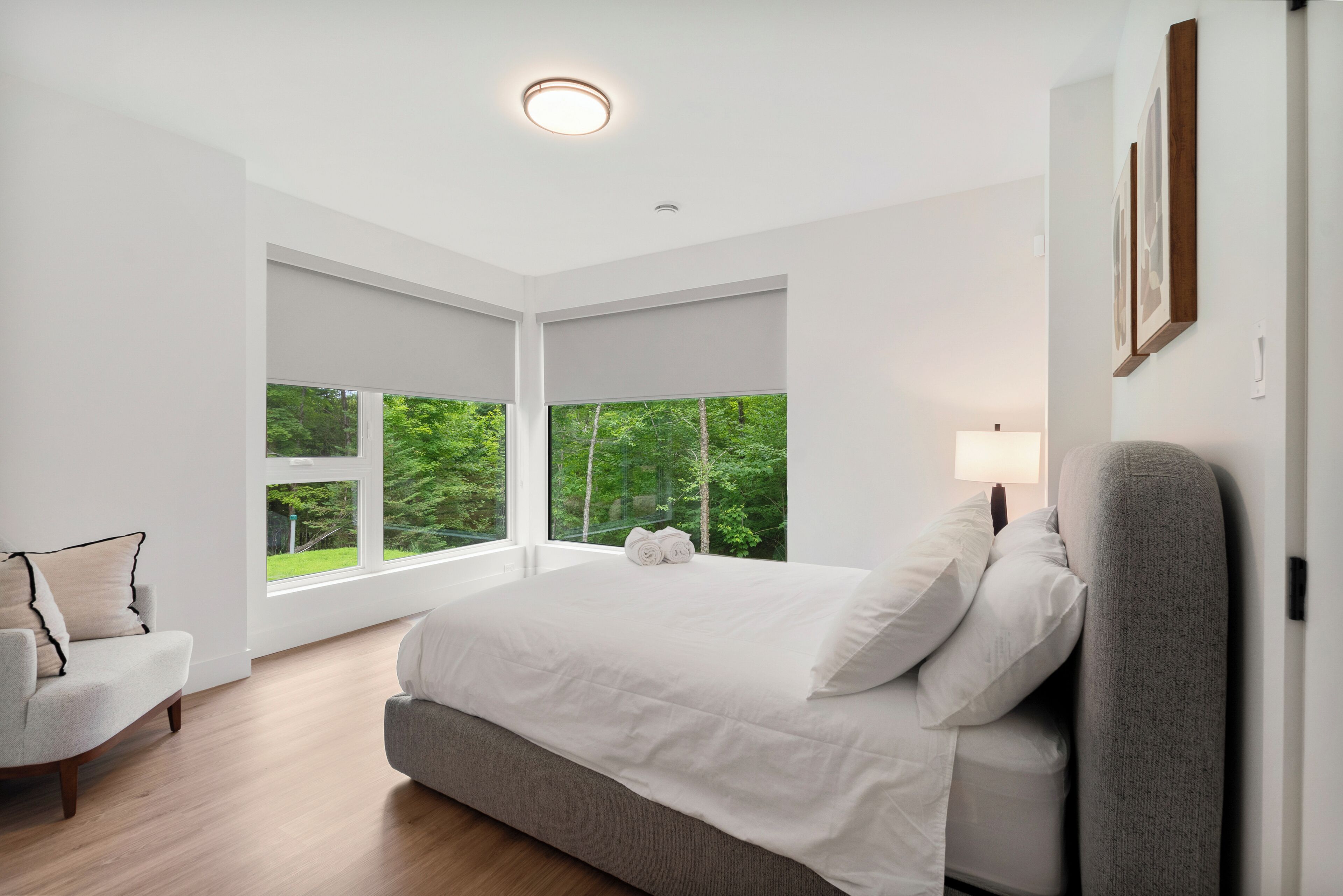 Un dormitorio moderno con una cama grande, una silla y vistas a la vegetación a través de amplios ventanales.