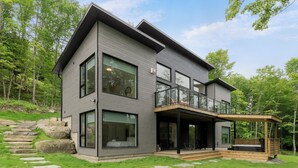 Une maison moderne à deux étages, dotée de grandes fenêtres, d’un balcon et d’un chemin en pierre menant à l’entrée.