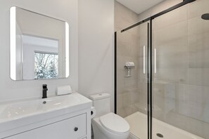 A modern bathroom with a white vanity, a toilet, and a glass-enclosed shower. - Chalet Solea by Tremblant Platinum (la conception)