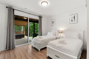 A bedroom with two beds, a sliding glass door to a deck, and a ceiling light. - Chalet Solea by Tremblant Platinum (la conception)